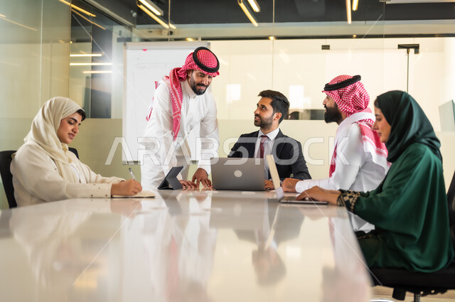 Discussing and organizing work among Saudi Gulf Arab employees in the meeting room, agreeing on commercial projects, a comfortable work environment in Saudi companies, using modern technical devices in offices, completing practical tasks via a laptop.