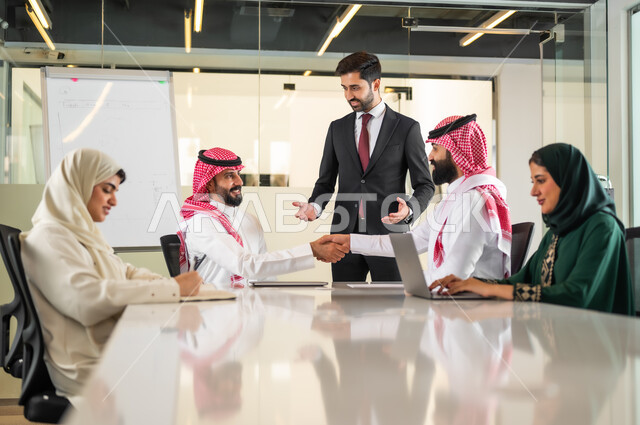 Group interaction and unity to achieve the company’s goals and solve problems, shaking hands and concluding new business agreements and deals, analyzing and studying new projects, using the blackboard to explain the processes and procedures followed in the company, a Saudi-Gulf Arab team in a meeting inside the office.