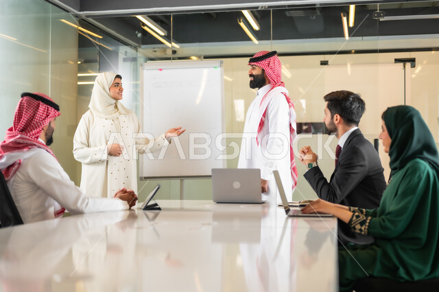 Using the blackboard to explain the processes and procedures followed in the company, teamwork and team spirit, discussing work plans, ensuring a clear and comprehensive understanding of the business, using the laptop to take notes, professionalism and dedication to achievement, a Saudi Gulf Arab team in a meeting,