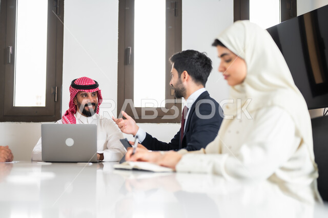 ايماءات السعادة والسرور لبدء الشراكة، بيئة العمل المريحة في الشركات السعودية, اجتماع عمل بين موظفين عرب خليجيين سعوديين في غرفة الاجتماعات، نقاشات خاصة بالعمل,التفاهم والتعاون بين الزملاء لتحقيق أهداف الشركة, استخدام الأجهزة التقنية الحديثة في المكاتب