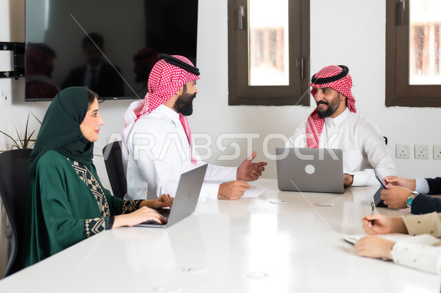 نقاشات خاصة بالعمل, استخدام الأجهزة التقنية الحديثة في المكاتب، التفاهم والتعاون بين الزملاء لتحقيق أهداف الشركة, ايماءات السعادة والسرور لبدء الشراكة، اجتماع عمل مع موظفين عرب خليجيين سعوديين في غرفة الاجتماعات، بيئة العمل المريحة في الشركات السعودية,