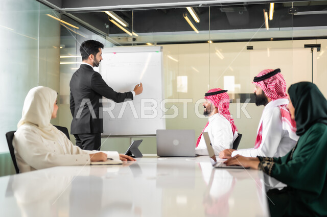 بيئة العمل المريحة في الشركات السعودية، استخدام الأجهزة التقنية الحديثة في المكاتب، استعمال السبورة لتوضيح الأفكار، اجتماع عمل بين موظفين عرب خليجيين سعوديين في غرفة الاجتماعات، التفاهم والتعاون بين الزملاء لتحقيق أهداف الشركة