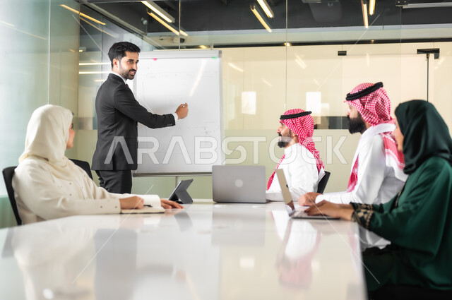 استخدام الأجهزة التقنية الحديثة في المكاتب، استعمال السبورة لتوضيح الأفكار، اجتماع عمل بين موظفين عرب خليجيين سعوديين في غرفة الاجتماعات، التفاهم والتعاون بين الزملاء لتحقيق أهداف الشركة, بيئة العمل المريحة في الشركات السعودية