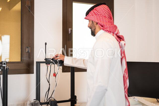 التجهيز لإجراء (بودكاست) عبر مواقع التواصل الاجتماعي في الاستوديو، التحضير لعمل البث المباشر و تشغيل الاجهزه الالكترونيه, شاب عربي خليجي سعودي يرتدي الزي التقليدي والشماغ يقوم بربط الأسلاك بجهاز الحاسوب