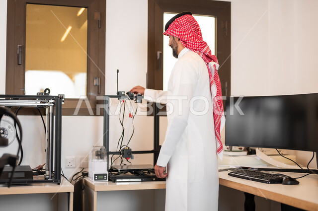 Operating electronic devices and preparing for live broadcasting. A young Saudi Gulf Arab man wearing traditional clothing and a shemagh connects wires to the computer. Preparing to conduct a podcast via social networking sites in the studio.