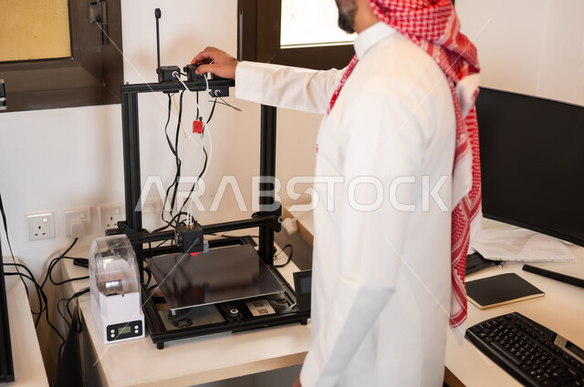 التحضير لعمل البث المباشر و تشغيل الاجهزه الالكترونيه, شاب عربي خليجي سعودي يرتدي الزي التقليدي والشماغ يقوم بربط الأسلاك بجهاز الحاسوب، التجهيز لإجراء (بودكاست) عبر مواقع التواصل الاجتماعي في الاستوديو