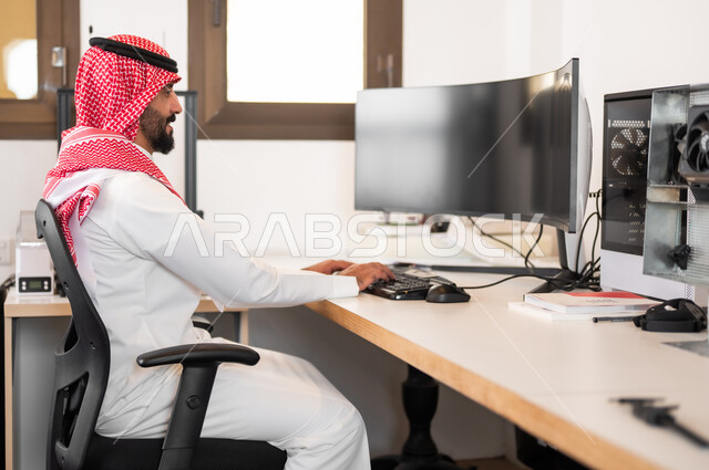 إجراء بث مباشر (بودكاست) عبر مواقع التواصل الإجتماعي، مفهوم إدمان الإنترنت والأجهزة الإلكترونية الحديثة، صورة من الجانب لشاب عربي خليجي سعودي يرتدي الزي التقليدي والشماغ يلعب ألعاب الفيديو على جهاز الكمبيوتر