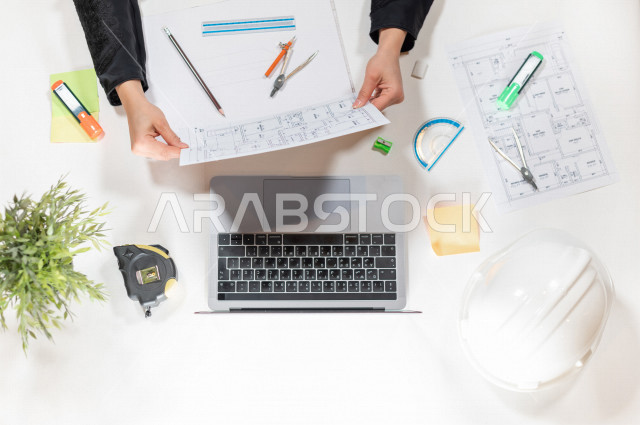  تصوير مقرب من الأعلى , لمهندسة تصميم داخلي عربية سعودية , مهندسة تصمم الأثاث الداخلي أمام اللابتوب على مكتب أبيض , وظيفه ومهن , بيئة عمل , خلفية بيضاء .