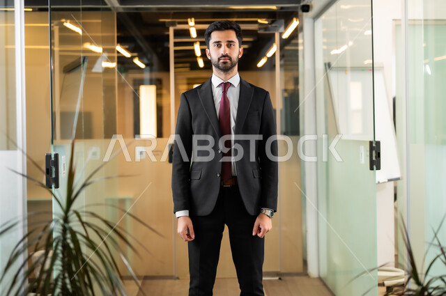العمل في الشركات السعودية الراقية, إدارة وتنظيم الأعمال ضمن مقر الشركة, رجل أعمالي يرتدي الزي الرسمي يقف بإستقامة ويينظر إلى الكاميرا , مهن ووظائف إدارية, الاحترافية والتفاني في العمل