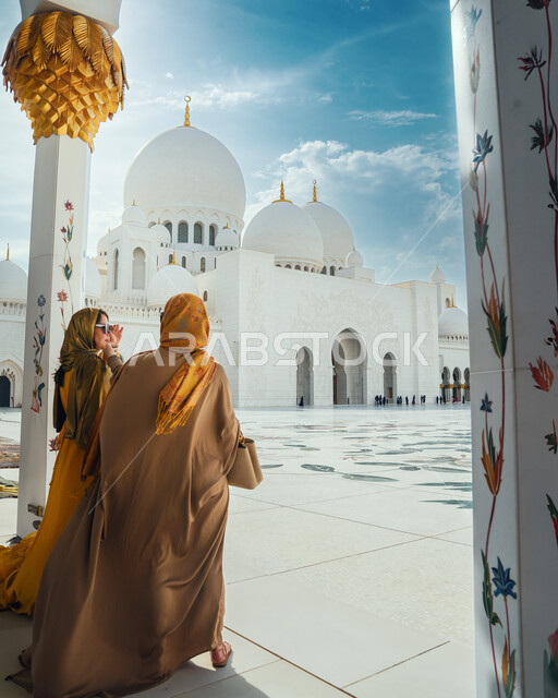 Famous sacred religious landmarks and places, a picture from the back of two Arab Gulf and Emirati women standing in the sanctuary of the Sheikh Zayed Grand Mosque in the Emirate of Abu Dhabi in the United Arab Emirates, architectural engineering art and Islamic architectural designs