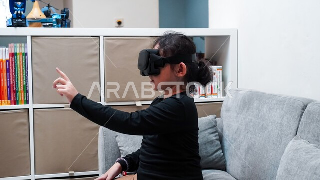 قضاء أوقات ممتعة بمتابعة أفلام الكرتون عبر نظارة الواقع الافتراضي، صورة مقربة لفتاة عربية خليجية سعودية ترتدي نظارات ثلاثية الأبعاد تقوم بالإشارة الى شيئ ما، التفاعل والإندماج مع العالم الخيالي، لعب ألعاب الفيديو ومشاهدة رسومات متحركة