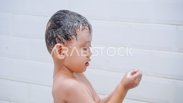 Protecting the scalp from dandruff and cleaning it, the concept of bathing with warm water, care and attention to personal hygiene, a close-up picture of a Saudi Arabian Gulf boy washing his hair with soap and water in the bathroom, a feeling of relaxation and comfort.