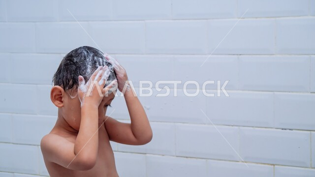 قضاء وقت ممتع باللعب برغوة الصابون، الحفاظ على النظافة الشخصية، صورة مقربة لولد عربي خليجي سعودي يقوم بغسل شعره بالمياه الدافئة داخل الحمام، ايماءات السعادة والسرور للاستحمام بالماء الساخن، تنظيف فروة الرأس وحمايتها من القشرة