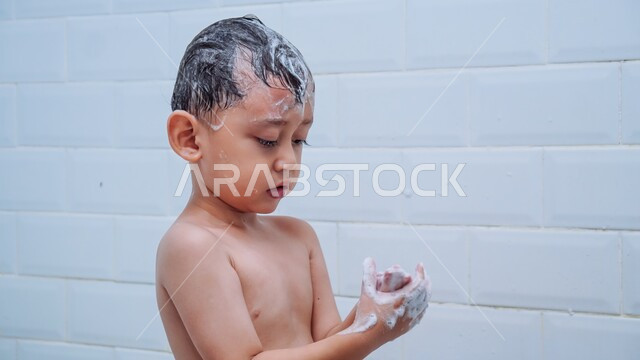 الحفاظ على النظافة الشخصية، قضاء وقت ممتع باللعب برغوة الصابون، صورة مقربة لولد عربي خليجي سعودي يقوم بغسل شعره بالمياه الدافئة داخل الحمام، ايماءات السعادة والسرور للاستحمام بالماء الساخن، تنظيف فروة الرأس وحمايتها من القشرة