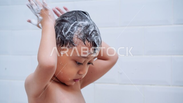 الاستمتاع واللعب برغوة الصابون، الحفاظ على النظافة الشخصية، صورة مقربة لولد عربي خليجي سعودي يقوم بغسل شعره بالمياه الدافئة داخل الحمام، ايماءات السعادة والسرور للاستحمام بالماء الساخن، تنظيف فروة الرأس وحمايتها من القشرة