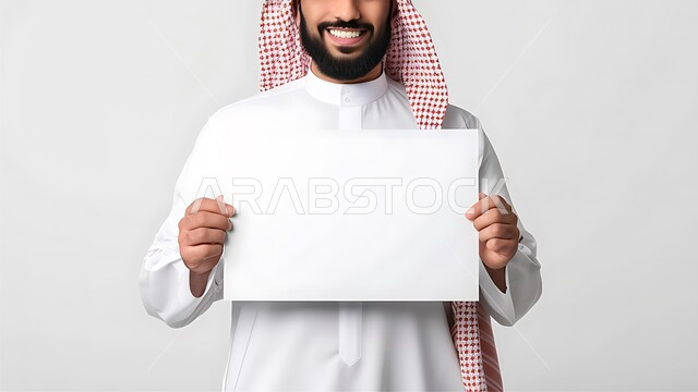 استخدام لوحات توضيحية ووسائل تعليمية، إعلانات وعروض تسويقية، موك اب مربع أبيض، بورتريه مقرب لشاب عربي خليجي سعودي مبتسم يرتدي الزي التقليدي والشماغ يحمل بيده لوحه بيضاء مربعه فارغة، خلفية بيضاء