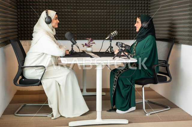 ايماءات الفرح والسرور, سيدتان عربيتان خليجيتان محجبتان مبتسمتان ترديان العباءة وسماعة الرأس, مقابلة عمل داخل الاستديو, معدات وأجهزة تسجيلات الصوت، اجراء بث صوتي مباشر (بودكاست) عبر برامج التواصل الاجتماعي
