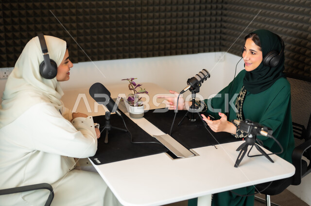 تعابير السعادة والسرور، سيدتان عربيتان خليجيتان محجبتان مبتسمتان ترديان العباءة وسماعة الرأس, مقابلة عمل داخل الاستديو، معدات وأجهزة تسجيلات الصوت، اجراء بث صوتي مباشر (بودكاست) عبر برامج التواصل الاجتماعي، ايماءات تدل على الحماس