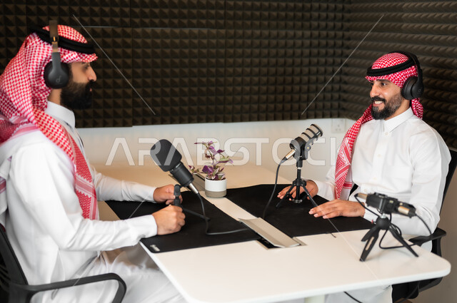ايماءات الفرح والسرور، رجلان عربيان سعوديان خليجيان مبتسمان يرتديان الزي التقليدي والشماغ و سماعة الرأس، مقابلة العمل داخل الأستديو، معدات وأجهزة تسجيلات الصوت، اجراء بث صوتي مباشر (بودكاست) عبر برامج التواصل الاجتماعي