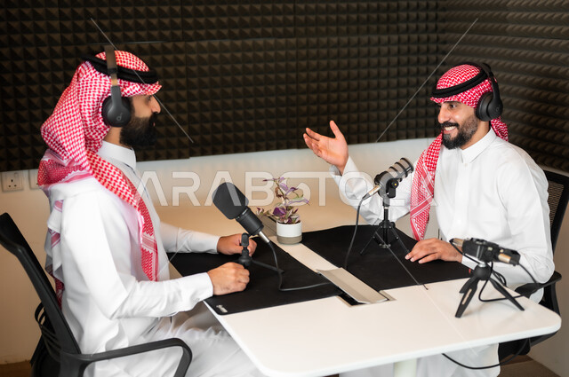 ايماءات الحماس والتفاعل، رجلان عربيان سعوديان خليجيان مبتسمان يرتديان الزي التقليدي والشماغ و سماعة الرأس، مقابلة العمل داخل الأستديو، معدات وأجهزة تسجيلات الصوت، اجراء بث صوتي مباشر(بودكاست) عبر برامج التواصل الاجتماعي، تعابير السعادة والسرور