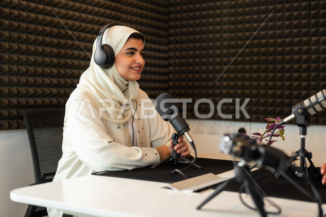 معدات وأجهزة تسجيلات الصوت، استديو تسجيل صوتي، امرأة عربية خليجية سعودية مبتسمة ترتدي الحجاب والعباءة، في مقابلة عمل داخل مقر الشركة، اجراء بث صوتي مباشر (بودكاست) عبر برامج التواصل الاجتماعي