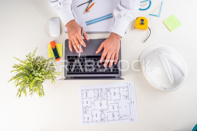  تصوير مقرب من الأعلى , لمهندس معماري خليجي , مهندس يعمل على تصميم العمارات من خلال اللابتوب على مكتب أبيض , وظيفه ومهن , بيئة عمل , خلفية بيضاء .