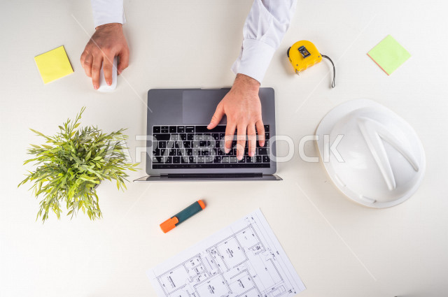  تصوير مقرب من الأعلى , لمهندس معماري خليجي , مهندس يعمل على تصميم العمارات من خلال اللابتوب على مكتب أبيض , وظيفه ومهن , بيئة عمل , خلفية بيضاء .
