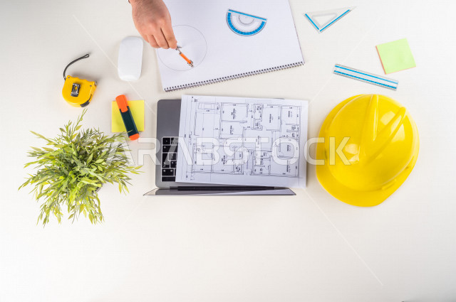  تصوير مقرب من الأعلى , لمهندس معماري خليجي , مهندس يعمل على تصميم العمارات من خلال اللابتوب على مكتب أبيض , وظيفه ومهن , بيئة عمل , خلفية بيضاء .