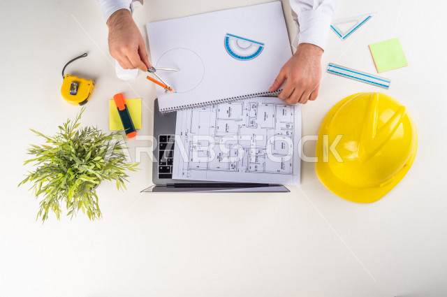  تصوير مقرب من الأعلى , لمهندس معماري خليجي , مهندس يعمل على تصميم العمارات من خلال اللابتوب على مكتب أبيض , وظيفه ومهن , بيئة عمل , خلفية بيضاء .
