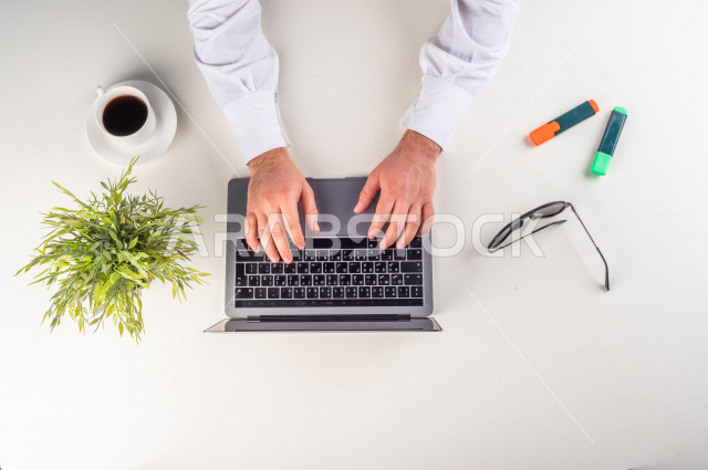 صورة مقربة من الأعلى , لمدير شركة يعمل من خلال اللابتوب على مكتب أبيض  , بيئة عمل , مهن ووظيفة , خلفية بيضاء .