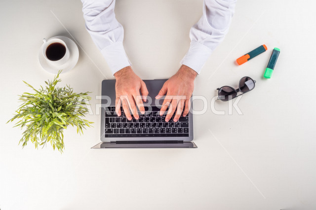 صورة مقربة من الأعلى , لمدير شركة يعمل من خلال اللابتوب على مكتب أبيض  , بيئة عمل , مهن ووظيفة , خلفية بيضاء .