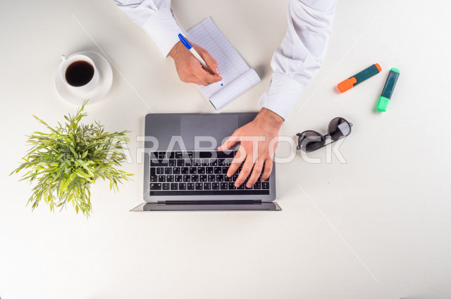 صورة مقربة من الأعلى , لمدير شركة يعمل من خلال اللابتوب على مكتب أبيض  , بيئة عمل , مهن ووظيفة , خلفية بيضاء .
