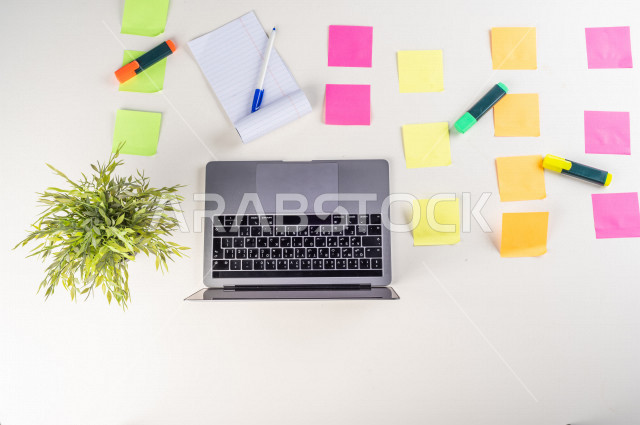 صورة مقربة من الأعلى , لموظف سعودي عربي يعمل من خلال اللابتوب على مكتب أبيض , مهن ووظيفة , بيئة عمل , خلفية بيضاء .