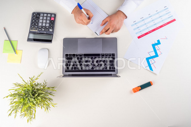 Close-up photo from the top, of a Saudi Arab man with stock experience, working on a laptop on a white desk, jobs and professions, work environment, white background.