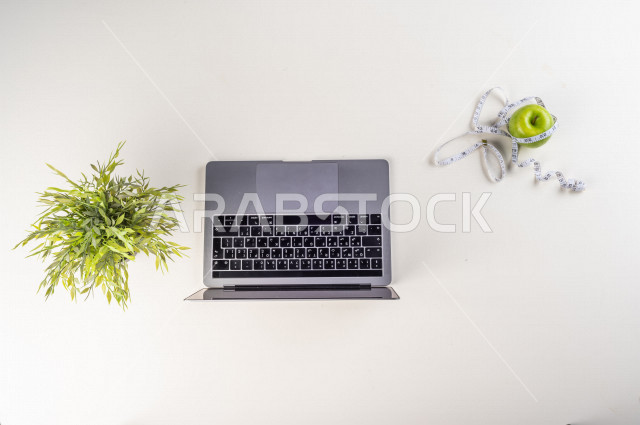 صورة مقربة من الأعلى , لأخصائي تغذية يعمل من خلال اللابتوب على مكتب أبيض , مهنة ووظيفة , بيئة عمل , خلفية بيضاء . 