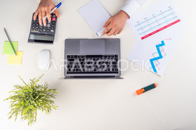 Close-up photo from the top, of a Saudi Arab man with stock experience, working on a laptop on a white desk, jobs and professions, work environment, white background.