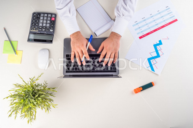  تصوير مقرب من الأعلى , لرجل عربي سعودي لديه خبره بالأسهم , يعمل من خلال اللابتوب على مكتب أبيض , وظيفه ومهن , بيئة عمل , خلفية بيضاء .