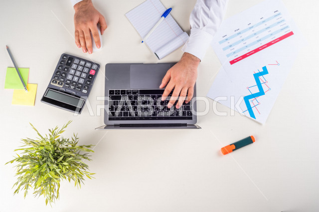  تصوير مقرب من الأعلى , لرجل عربي سعودي لديه خبره بالأسهم , يعمل من خلال اللابتوب على مكتب أبيض , وظيفه ومهن , بيئة عمل , خلفية بيضاء .