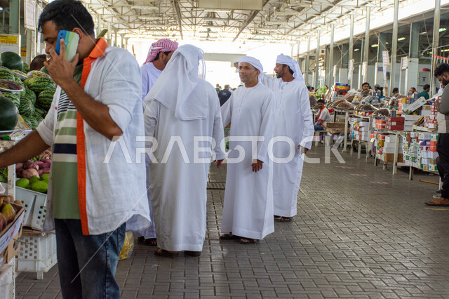 Customers gather to buy food commodities, local and national UAE agricultural crops and products, agricultural harvest season in the Emirate of Abu Dhabi, interest in local agriculture and self-sufficiency in the United Arab Emirates, popular markets for selling fresh vegetables and fruits in the city of Al Ain.
