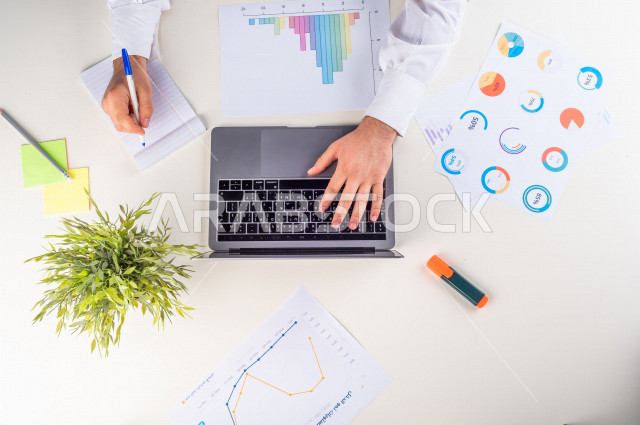  تصوير مقرب من الأعلى , لرجل عربي سعودي لديه خبره بالأسهم , يعمل من خلال اللابتوب على مكتب أبيض , وظيفه ومهن , بيئة عمل , خلفية بيضاء .
