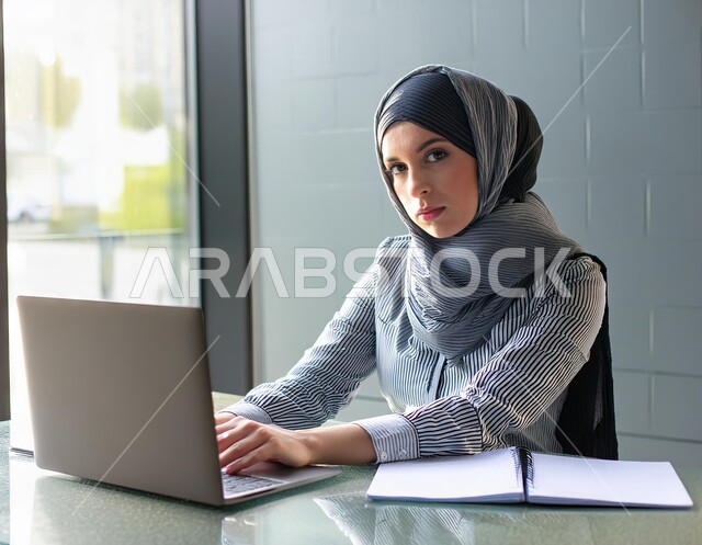 التفكير في حل المشكلات وشرود الذهن , التعب من ضغوطات العمل, موظفة عربية خليجية سعودية محجبة تعمل على جهاز الحاسوب المحمول بإيماءات الحزن والضجر, مهن ووظائف مكتبية نسائية, إدارة شؤون الأعمال وتنظيمها في مقر الشركة