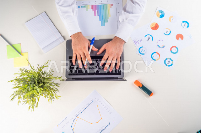  تصوير مقرب من الأعلى , لرجل عربي سعودي لديه خبره بالأسهم , يعمل من خلال اللابتوب على مكتب أبيض , وظيفه ومهن , بيئة عمل , خلفية بيضاء .