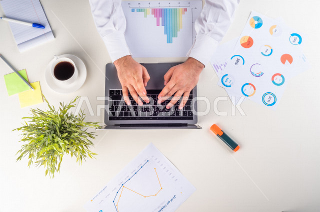  تصوير مقرب من الأعلى , لرجل عربي سعودي لديه خبره بالأسهم , يعمل من خلال اللابتوب على مكتب أبيض , وظيفه ومهن , بيئة عمل , خلفية بيضاء .