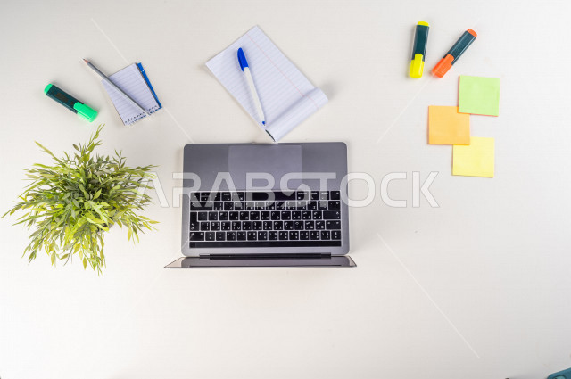 صورة مقربة من الأعلى , لموظف سعودي عربي يعمل من خلال اللابتوب على مكتب أبيض , مهن ووظيفة , بيئة عمل , خلفية بيضاء .