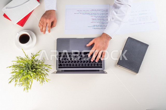 A close-up image from the top, of a Saudi Arab employee working on a laptop on a white desk, professions and jobs, a work environment, a white background.