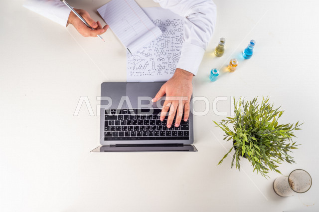 Close up from the top, of a chemistry professor working with his laptop on a white desk, working environment, white background.