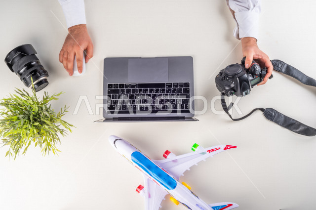 A close-up from the top, of a Saudi Arabian Gulf man putting flight ticket information on his laptop at the airport, working environment, white background