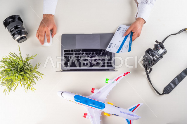 صورة مقربة من الأعلى , لرجل خليجي سعودي يضع معلومات تذاكر الرحلات الى اللابتوب في المطار , بيئة عمل , خلفية بيضاء .