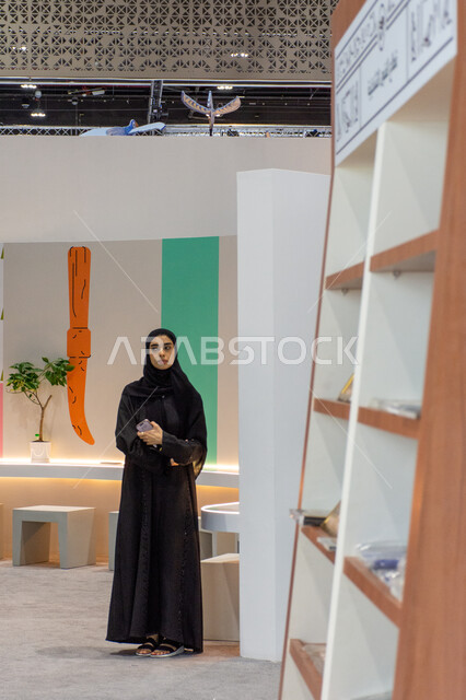 Cultural and entertainment sections and pavilions, the world of books and publishing, a veiled young Arab Gulf Emirati woman wearing a traditional abaya standing at the 2024 Abu Dhabi International Book Fair, exhibitions and events in the United Arab Emirates, famous tourist places and landmarks in the Emirate of Abu Dhabi.