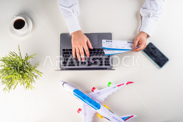 A close-up from the top, of a Saudi Arabian Gulf man putting flight ticket information on his laptop at the airport, working environment, white background